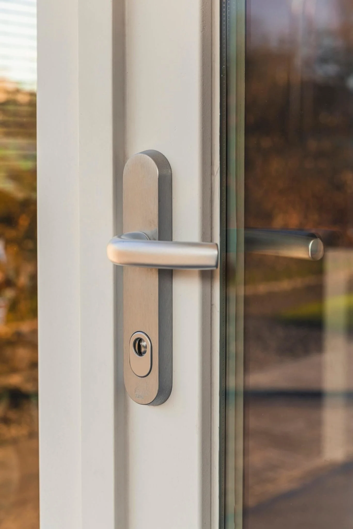 Detail van een aluminium veiligheidsschild met kruk op witte houten deur, voorzien van SKG** cilinder – Toelevering Online